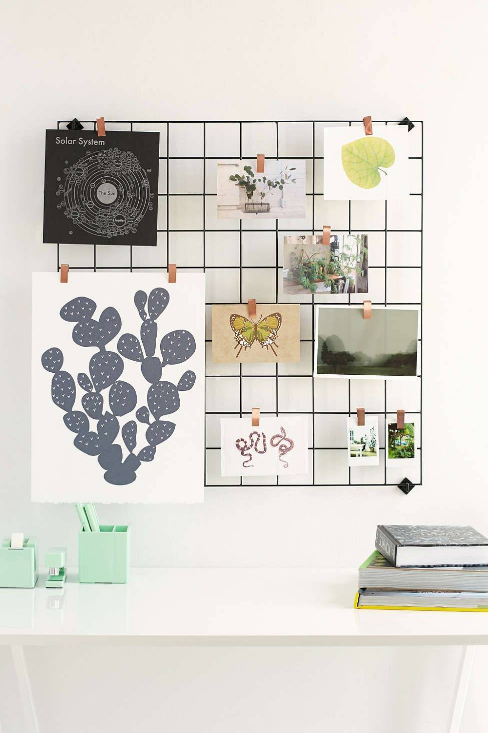 A wire rack to spend it on a wall acts like a bulletin board with various pieces of art on it.