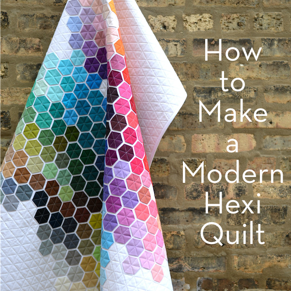A hexi quilt hanging folded in front of a weathered brick wall.