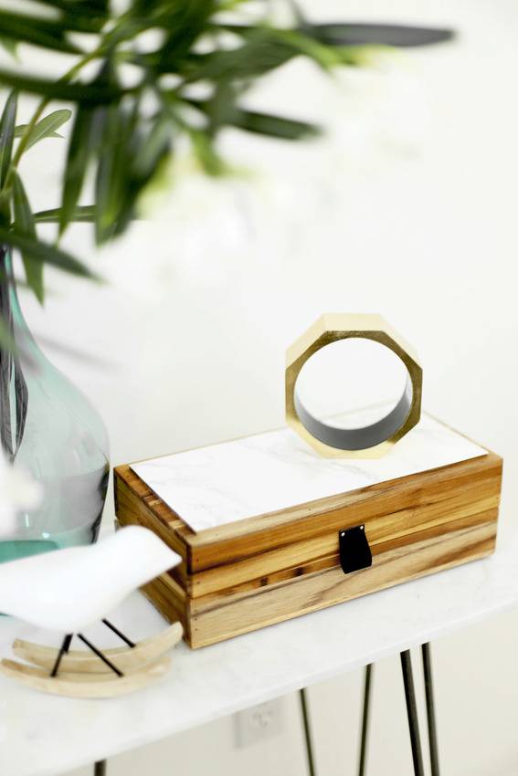 Small wooden box sitting on top of a white table next to a plant in a vase.