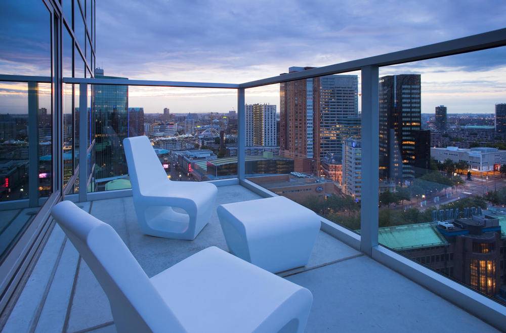 White chairs sitting on a balcony with glass walls facing a city skyline.