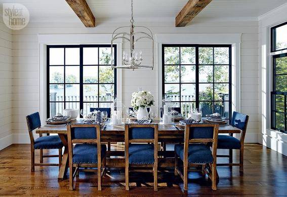 A large dining table with padded blue chairs in a white room with two large windows.