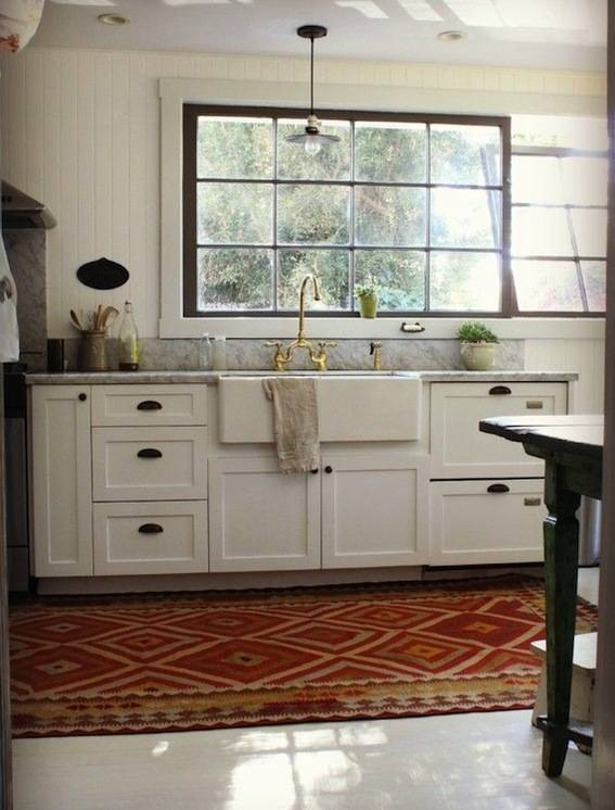 A red diamond rug on the floor of a white kitchen with a golden sink faucet.