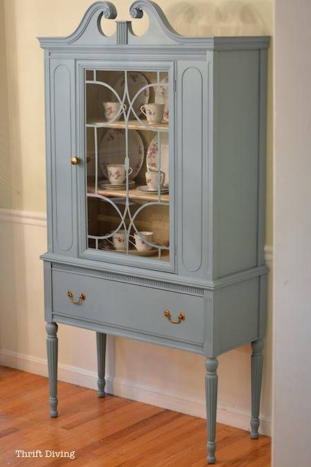 A light blue cabinet with a glass door is sitting on a wooden floor.