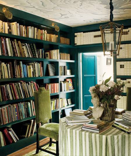 A green chair sits at a table in a room filled with books.