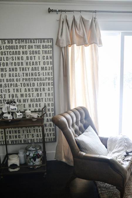 Sofa chair lying near a window and a table full of cups and jars.