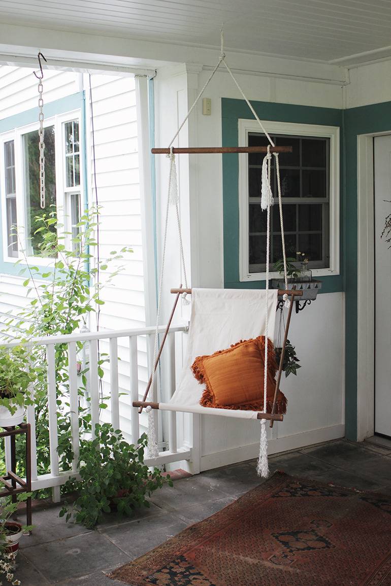 A swing on the porch of a house with white paint and green trim.