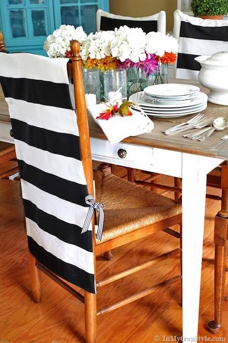 A black and white wide striped cloth over the back of a wooden chair in front of a table with white flowers in vases on it.