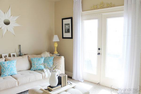 A white sofa with blue pillows sits in the corner of a room near a double door made of glass.