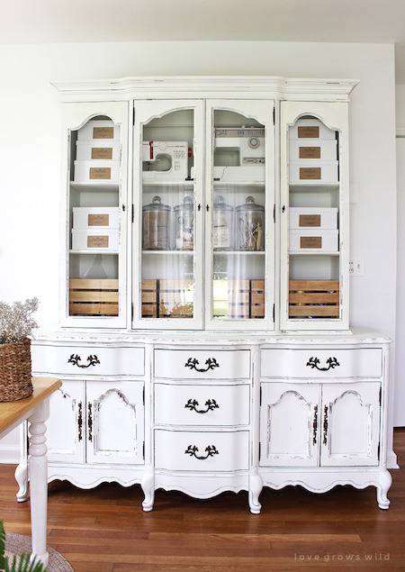 White hutch china cabinet sitting against a wall on top of a dark wood floor.