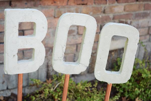 The capital letters B, O. O, each on a copper stick against a red brick wall.