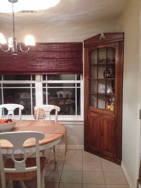 A dining room with a brown blind on the window and a brown display shelf in the corner.