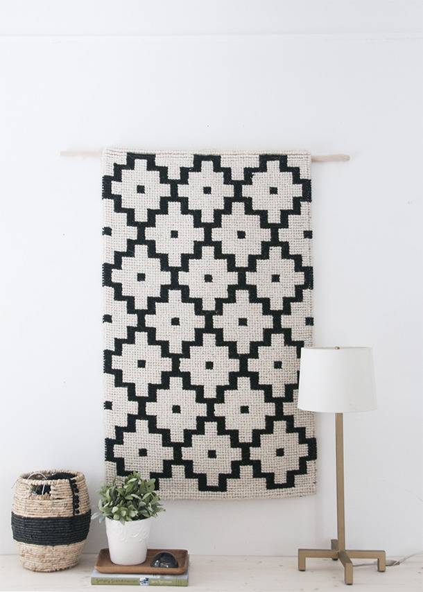 A black and white painting hanging on a white wall with a lamp and vase near it.