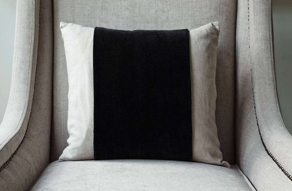 A pillow with a black stripe is sitting on a chair.