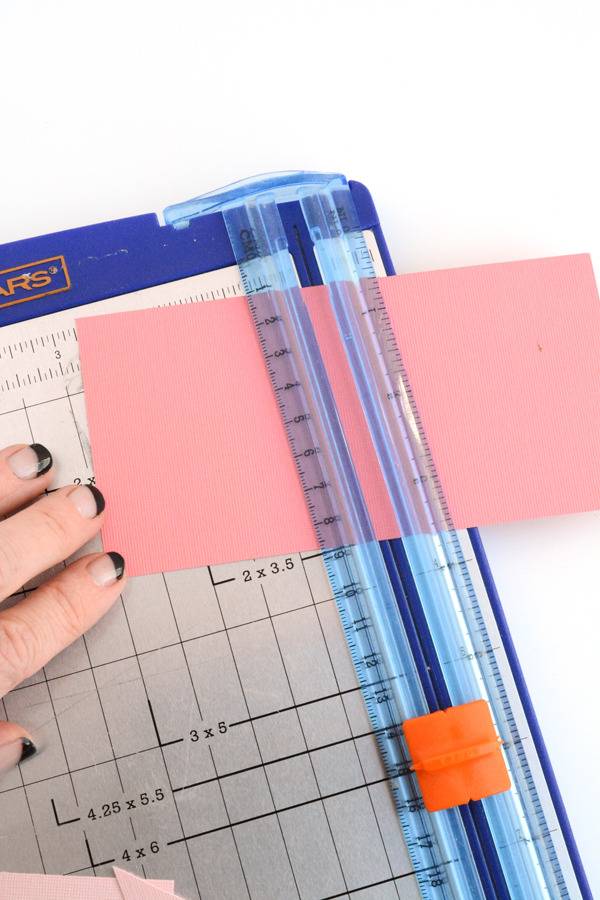 A person puts a pink paper under the ruler in a paper cutter.