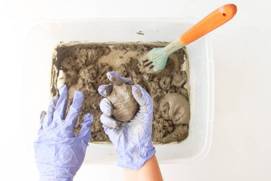 Man with gloves in hands is holding a piece of mud from a box of mud and spoon.