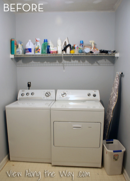 A washer and dryer in a small grey room under a shelf of cleaning supplies.