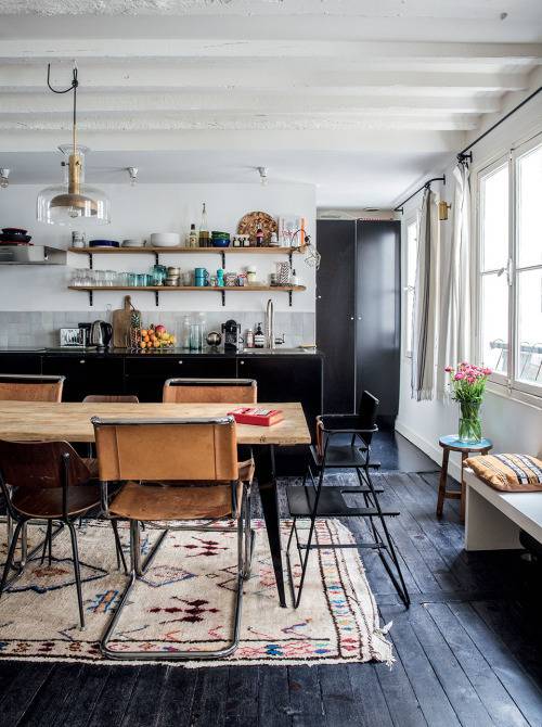 A wooden dining table on a tan rug laying on a black wooden floor.