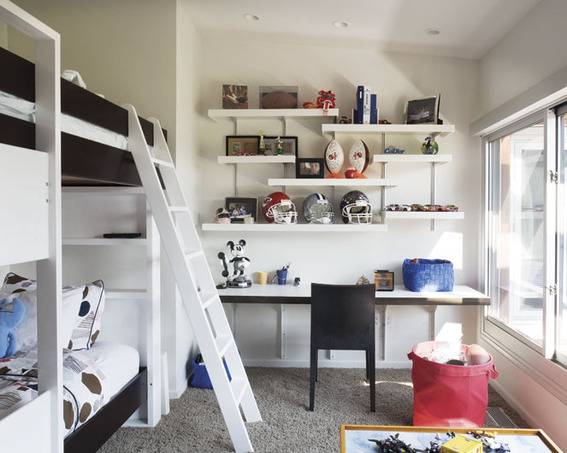 White shelves are staggered on a wall above a white desk next to a white bunk bed.