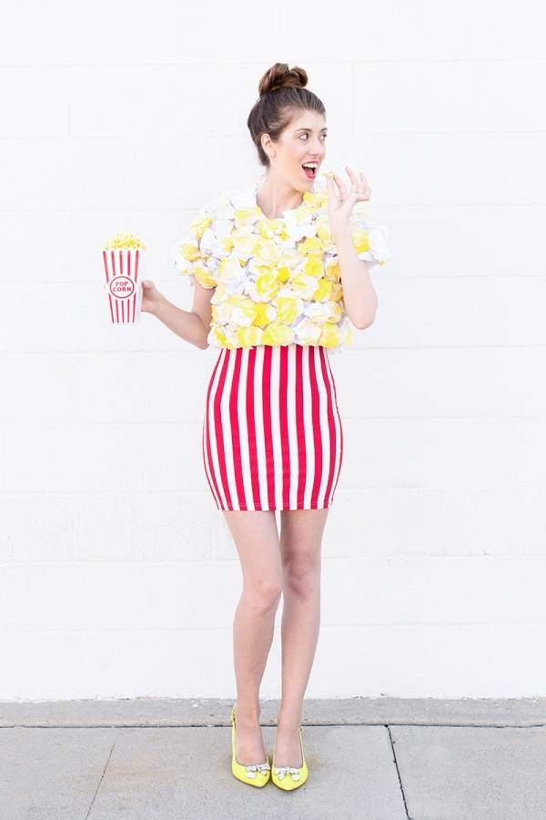 Woman wearing a red and white skirt and yellow top holding a small box of popcorn.