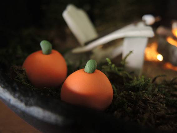 Two orange pumpkins with green stems made of clay sit on a black plate as a part of a centerpiece.