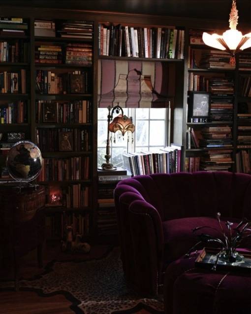 A room full if books on shelves and a purple couch.