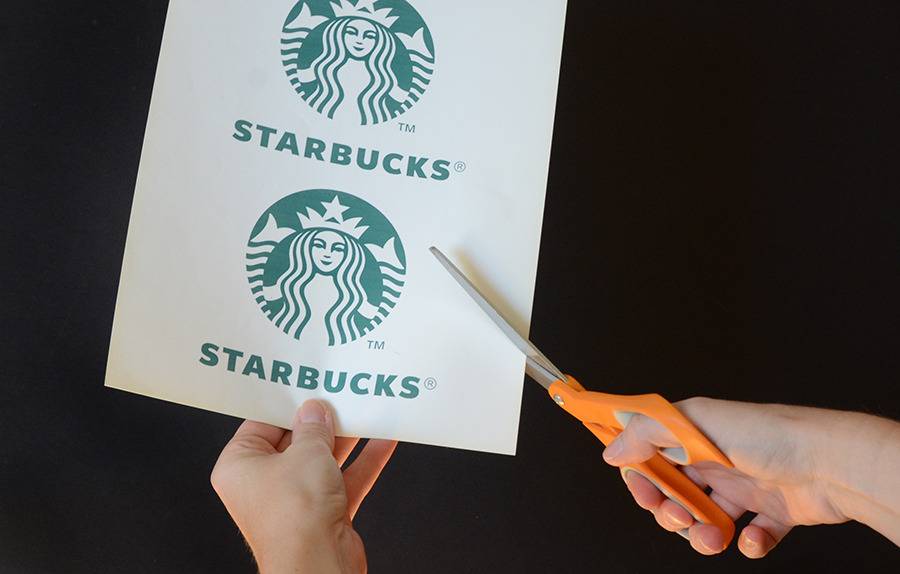 A person is cutting starbucks printed paper with orange scissor.