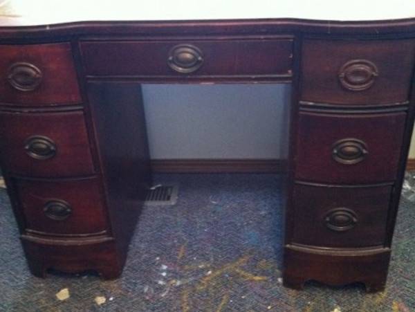 A dark brown desk with oval worn brass drawer handles.