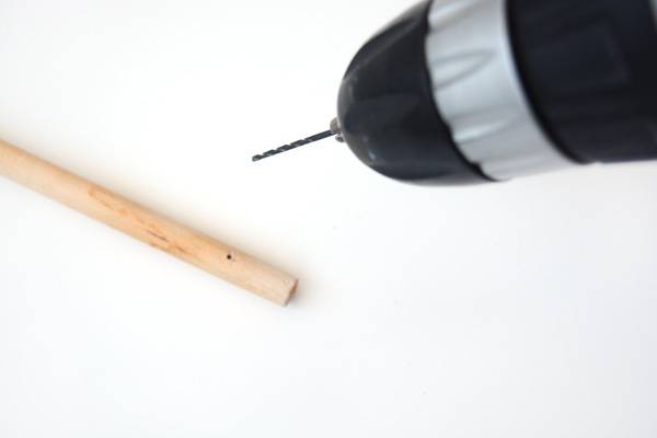 A person is using a drill on a small dowel rod.