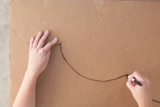 A right hand holding a black marker that has drawn a couple of troughs and a left hand holding down the cardboard.