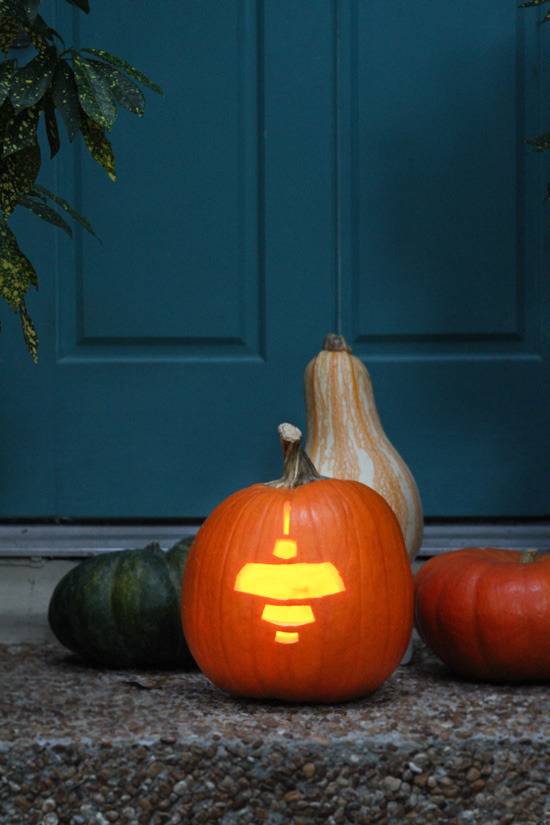 Pendant light carved into pumpkin on front door step near other gourds.