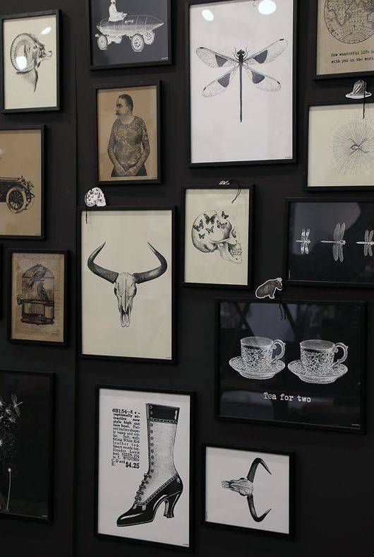 A black wall full of framed black and white drawings.