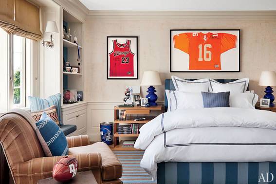 A sofa chair and a bed in a bedroom having two sports jersey paintings on the wall.