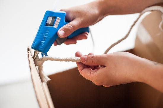 A person uses a glue gun to glue some rope to an item.