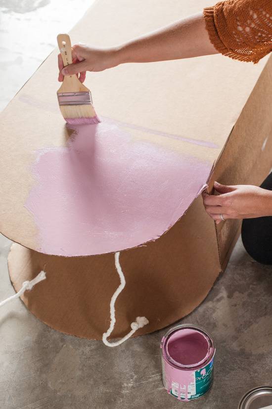 A woman painting  a piece of furniture pink with a wide paint brush.