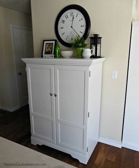 A white dresser with things on it sits under a black round clock.