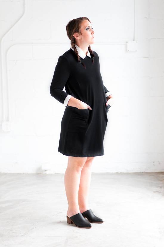 Woman with black dress and black shoes standing in front of the white wall.