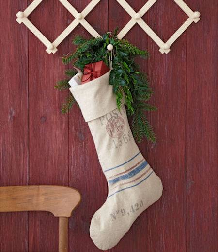 A sock with holly is hanging on a red wall.