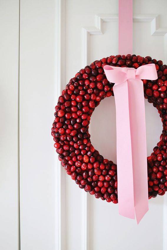 A red wreath made of small red balls that look like cranberries or cherries is hung with a long pink ribbon.
