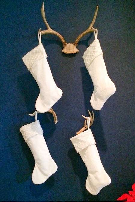 Four white stockings are hanging from a blue wall.