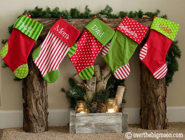 Five green, red and white stocking hanging from a tree trunk mantel over lit candles in a box of wood.