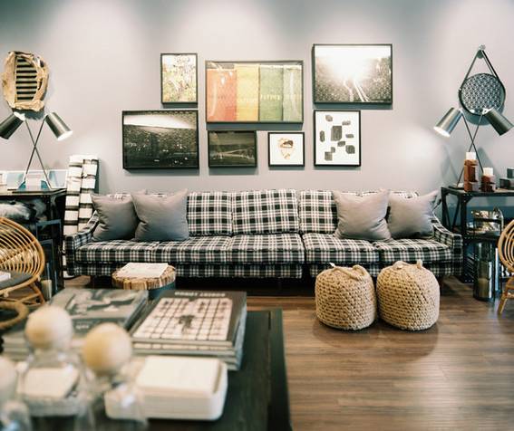 A long plaid sofa sits under several pieces of art in a room with grey walls.