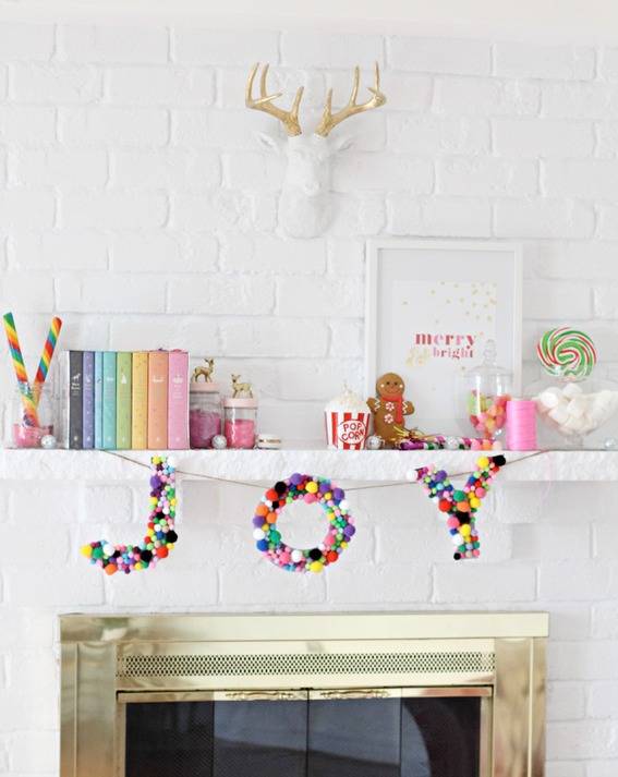 Various bright colored pom poms are used to spell out the letters joy to create a Garland above a fireplace.