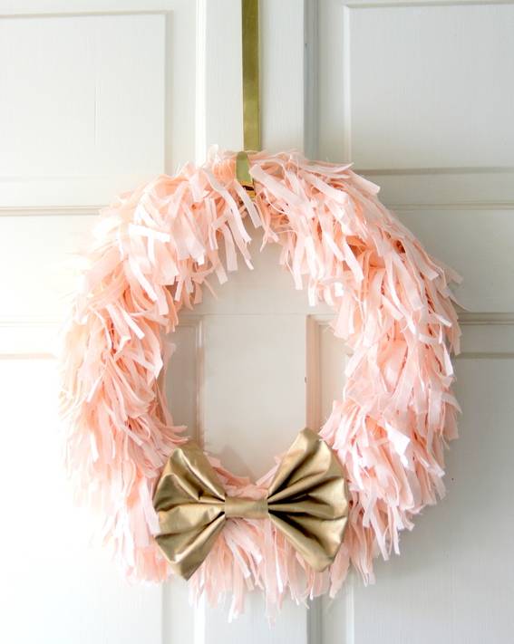 A pink wreath with a bow is hanging on a white wall.