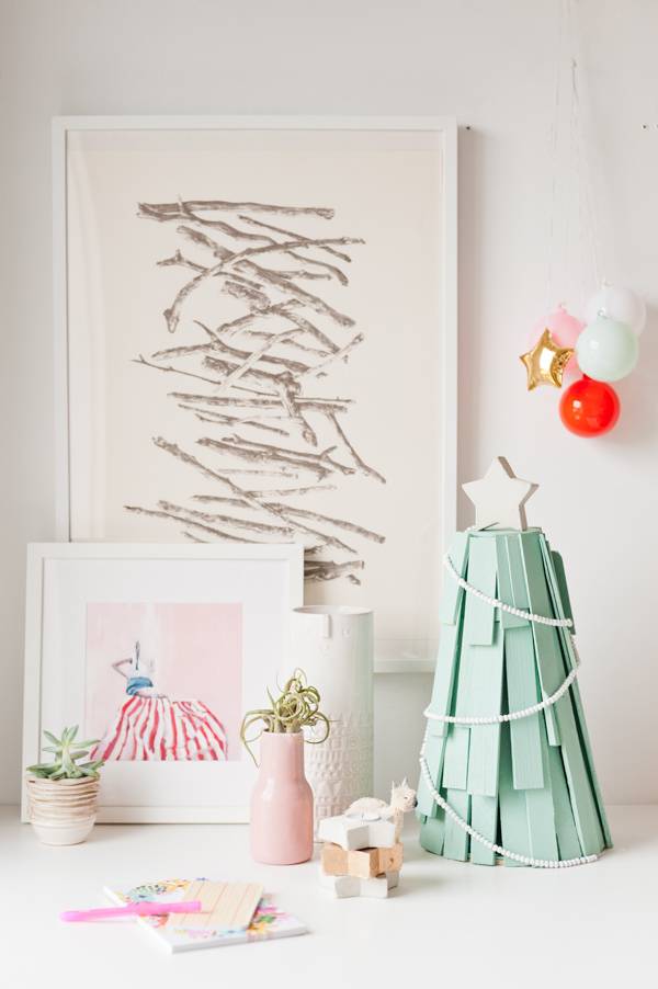 A scribbly drawing hangs on the wall in a room with a green Christmas tree.
