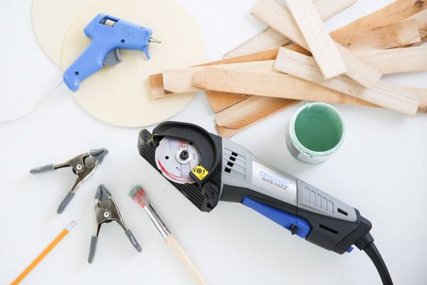 Cutter, clips, glue gun, paint brushes, paint bottle, wooden sticks are on the table.