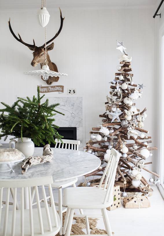 A Christmas tree sits in the corner near a window in a room with dining furniture.