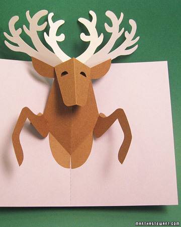 A cut out pop up of the front end of a brown reindeer with six white antlers on a green background.