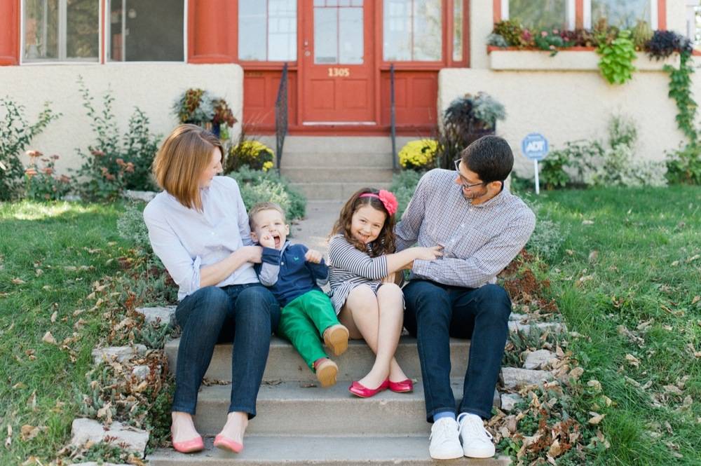 A mom and a father sitting on the house steps with a boy and girl in between them