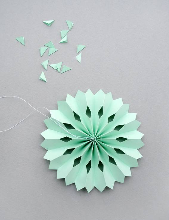 A very light green paper cutout of a sphere with diamond cut outs and the cut out pieces are laying next to it.