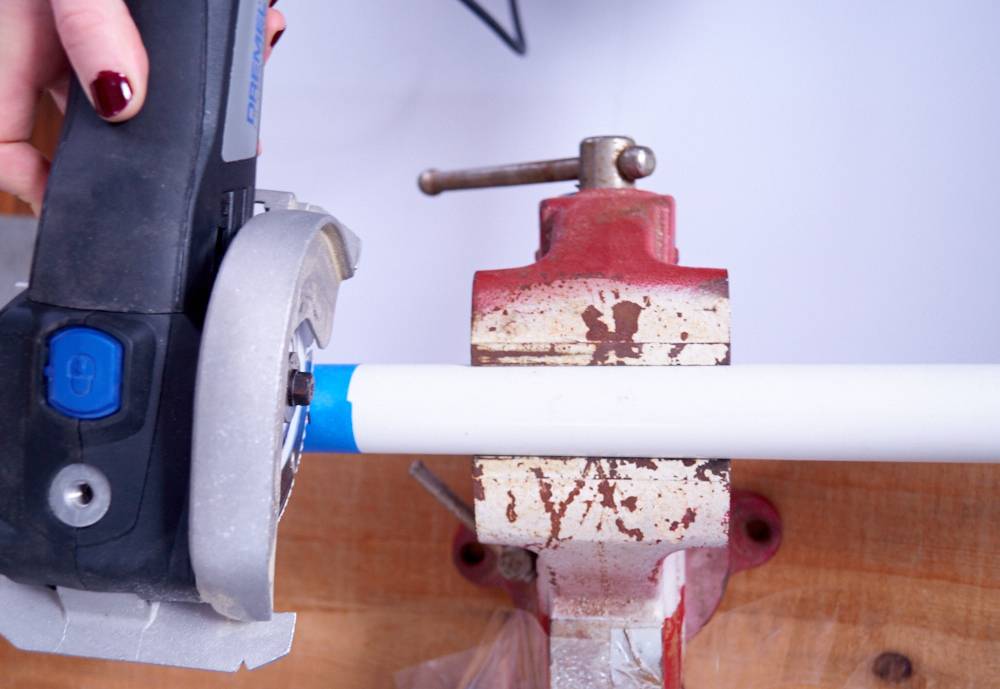 A white piece of pvc pipe in a vise is being cut by a small circular saw.